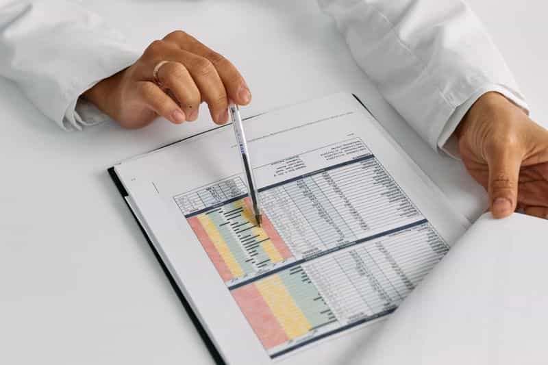 Hands holding a pen over a printed results table on a clipboard at a bright desk