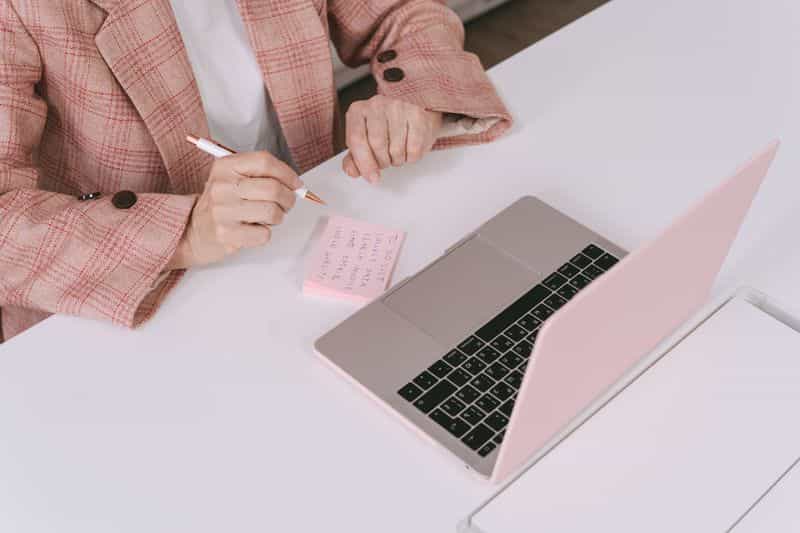 A person working at a laptop on a desk beside a notebook