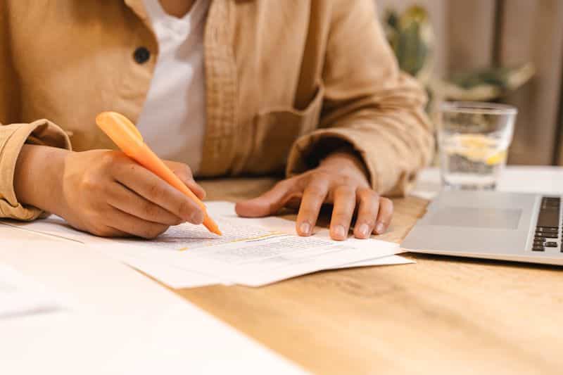 Close-up of a person sitting at a table writing handwritten notes on a sheet of paper