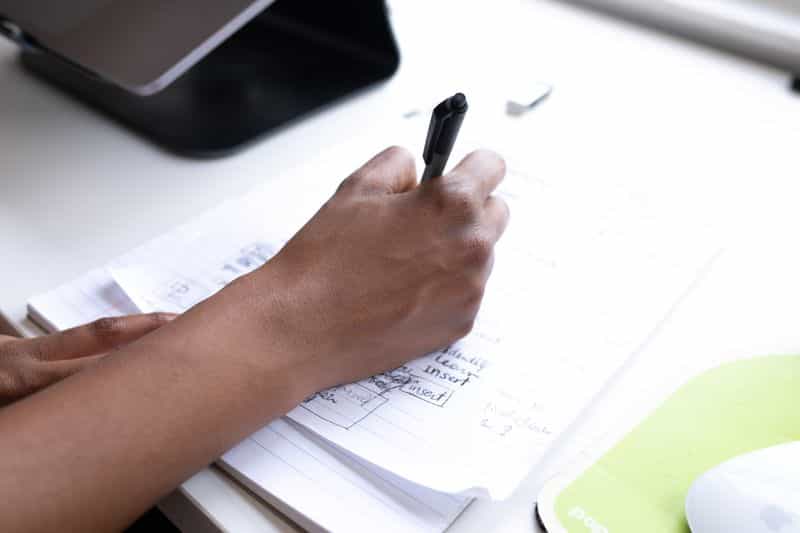 A person writing notes on paper at a desk while planning a research study