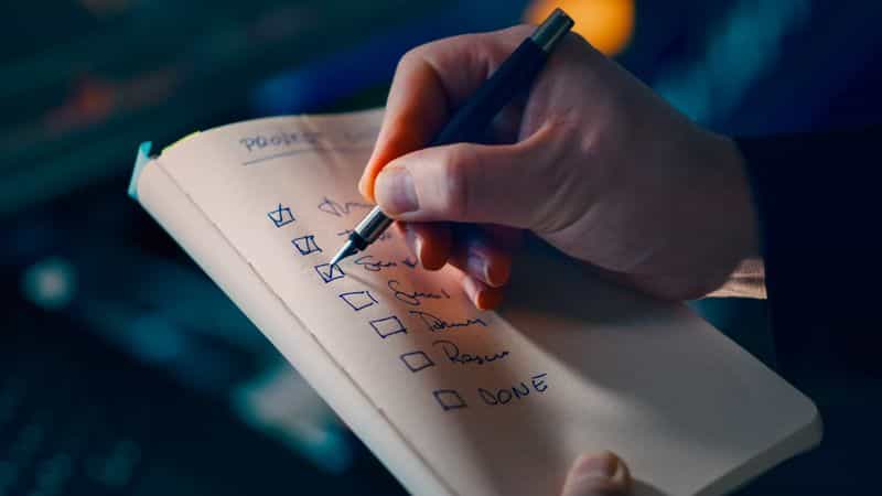 A hand writing a numbered checklist in a notebook while planning a research project