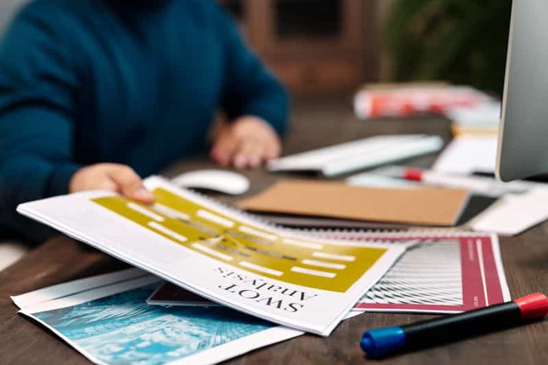 A person in a long sleeve top holding a printed page near a pen at a desk