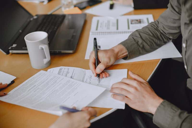 Close up of a person signing a printed document at a desk, pen in hand