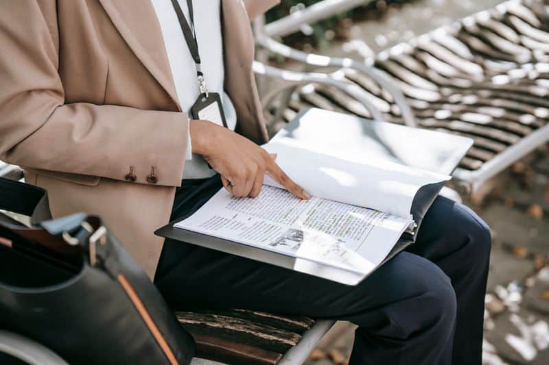 A person on a bench tracing a line of a printed document held in a folder on their lap