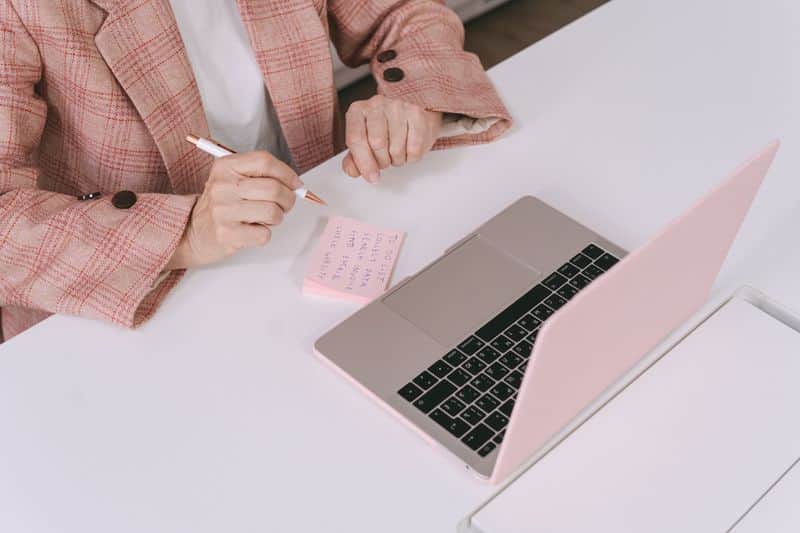 A person working at a laptop on a desk beside a notebook