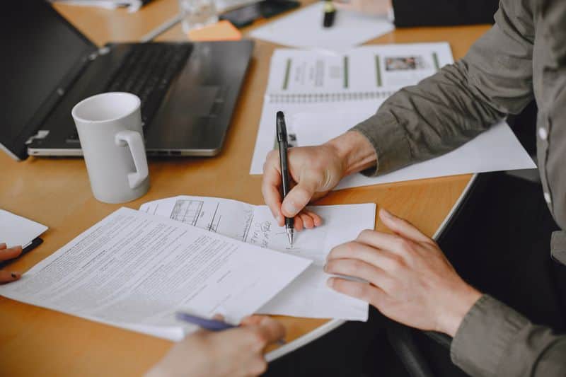 Close up of a person signing a printed document at a desk, pen in hand