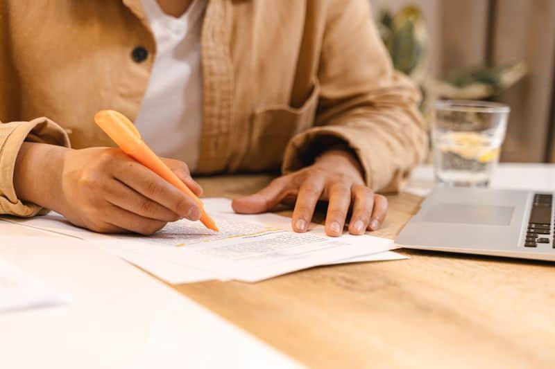 Close-up of a person sitting at a table writing handwritten notes on a sheet of paper